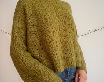 May include: A long-sleeved olive green crochet sweater featuring a ribbed crew neckline and cuffs. The garment is crafted with a repeating vertical pattern of openwork stitches and solid crochet columns, creating a textured, semi-sheer appearance.