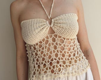 May include: A cream-colored crochet halter top featuring a central gold-tone ring connecting the two bust cups. The bodice is crafted with a dense stitch pattern, while the lower section displays an open, net-like crochet design with a scalloped hem.