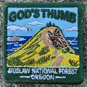 May include: A square embroidered patch featuring a landscape of a yellow and green hill against a blue sky and ocean. The text GOD'S THUMB is at the top, and SIUSLAW NATIONAL FOREST OREGON is at the bottom. The patch has a dark green border.