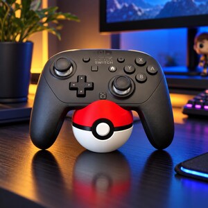 Op de afbeelding: Een zwarte Nintendo Switch Pro-controller die rust op een bolvormige rood-witte standaard met een Pokeball-thema. De controller is voorzien van analoge sticks, een richtingspad en knoppen met de labels X, Y, A en B.