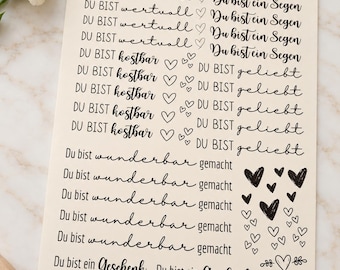 Könnte beinhalten: Ein cremefarbener Stickerbogen mit schwarzen deutschen Textzeilen wie DU BIST wertvoll, Du bist ein Segen, DU BIST kostbar, DU BIST geliebt, Du bist wunderbar gemacht und Du bist ein Geschenk, ergänzt durch verschiedene Herz-Symbole.