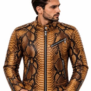 K&ouml;nnte beinhalten: Eine Jacke mit braun-schwarzem Schlangenledermuster, Stehkragen, zentralem silbernem Rei&szlig;verschluss und mehreren Rei&szlig;verschlusstaschen an Brust und Seiten. Das Kleidungsst&uuml;ck verf&uuml;gt &uuml;ber silberne Beschl&auml;ge, Schulterklappen und Rei&szlig;verschl&uuml;sse an den &Auml;rmelb&uuml;ndchen.