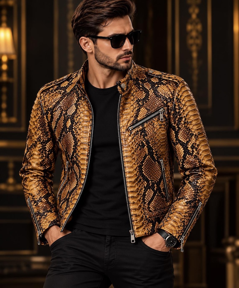 K&ouml;nnte beinhalten: Eine beigefarbene und schwarze Jacke mit Schlangenledermuster, Stehkragen, silberfarbenen Metallrei&szlig;verschl&uuml;ssen an der Vorderseite und an den &Auml;rmelb&uuml;ndchen sowie einem schwarzen T-Shirt darunter. Die Jacke hat eine strukturierte Oberfl&auml;che.