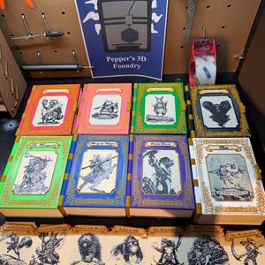 May include: Eight rectangular books with colourful covers and gold-toned filigree borders, each featuring a unique black and white animal illustration. Below the books are seven rectangular cards with matching animal art and titles.