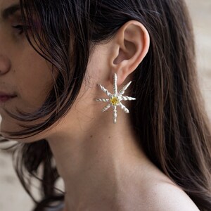 May include: A pair of silver star-shaped earrings with a yellow gemstone in the center of each star.
