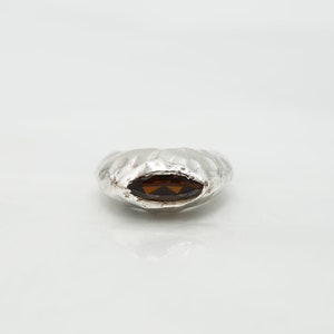 Puede incluir: Un anillo de plata con una superficie texturizada y una piedra preciosa ovalada marr&oacute;n.