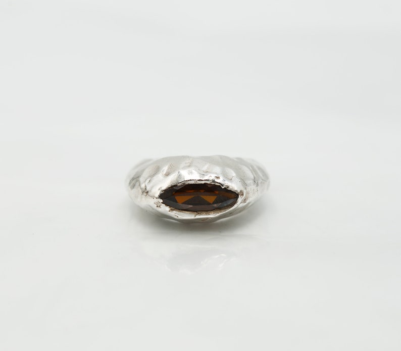 Puede incluir: Un anillo de plata con una superficie texturizada y una piedra preciosa ovalada marr&oacute;n.