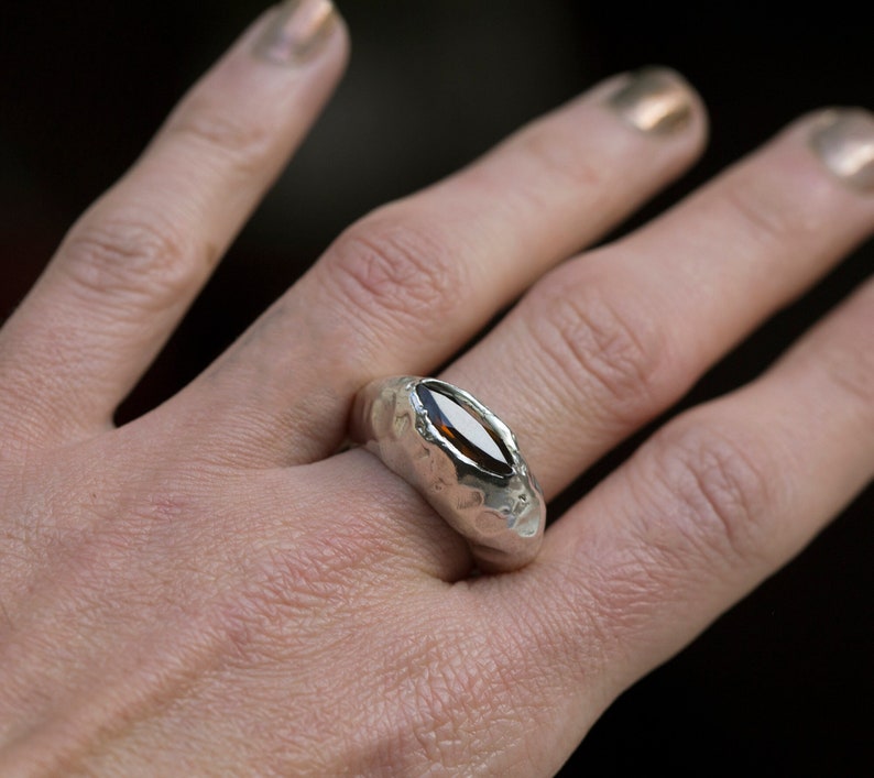 Puede incluir: Un anillo de plata con una banda texturizada y una piedra ovalada marr&oacute;n.