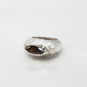 Puede incluir: Un anillo de plata con una piedra preciosa de forma marquesa marr&oacute;n engastada en el centro. El anillo tiene un acabado texturizado y martillado.