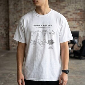 Op de afbeelding: Een wit t-shirt met een zwarte afbeelding getiteld Evolution of a Sim Racer. Het ontwerp toont zeven stadia van gaming-apparatuur, eindigend met een lege portemonnee en ramen, met tekst die elke stap van gamepad tot rig beschrijft.