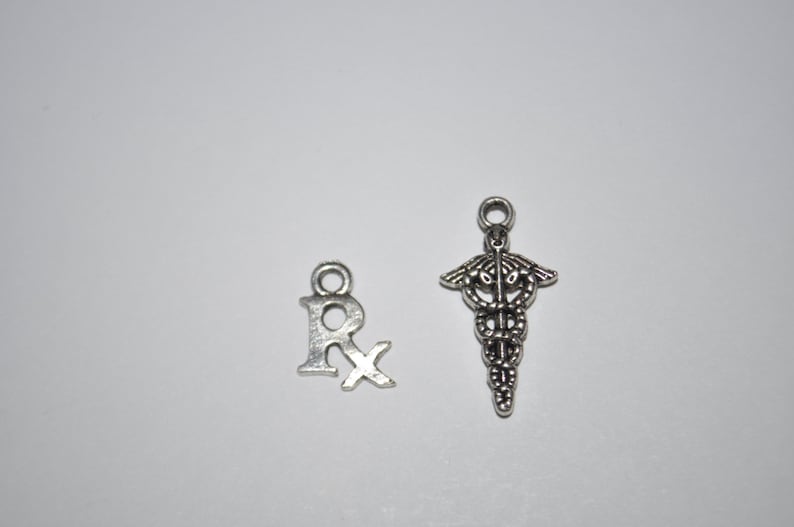 K&ouml;nnte beinhalten: Zwei silberne Anh&auml;nger, einer in Form des Buchstabens "R" mit einem Kreuz hindurch, der andere in Form einer Schlange, die um einen Stab gewickelt ist, ein Symbol der Medizin.