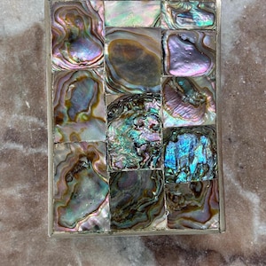May include: A rectangular metal frame containing a mosaic of iridescent abalone shell pieces. The shell segments display a variety of swirling colors including green, blue, purple, and pink, arranged in a grid-like pattern within the silver-toned border.