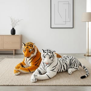 Könnte beinhalten: Zwei große Plüsch-Tiger, die auf einem strukturierten Teppich liegen. Ein Tiger ist orange mit schwarzen Streifen, der andere ist weiß mit schwarzen Streifen. Beide Stofftiere liegen in einer Ruheposition mit ausgestreckten Vorderpfoten.