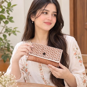 May include: A rectangular wallet featuring a two-tone design with a textured brown cork base and a white flap adorned with a repeating brown geometric star pattern. The wallet is secured with a single dark circular snap button closure.