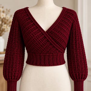May include: A deep burgundy long-sleeve sweater featuring a wrap-style V-neckline, a cropped length, and a wide ribbed hem. The garment is constructed with a textured knit pattern, including ribbed cuffs on the sleeves and a ribbed border along the neckline.
