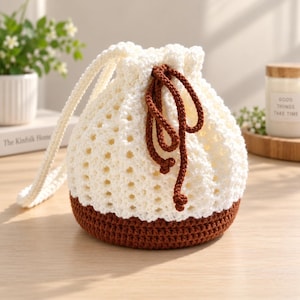 May include: A cream-colored crochet drawstring bag featuring a solid brown base and a matching brown cord closure. The upper portion of the bag is crafted with an openwork stitch pattern, while the base is made with a dense, solid stitch.