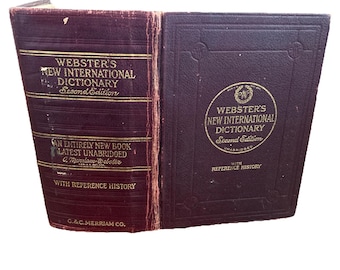May include: A dark maroon hardback book titled Webster's New International Dictionary Second Edition. The front cover and spine feature gold embossed text and decorative borders. The spine includes the publisher name G.&C. Merriam Co.