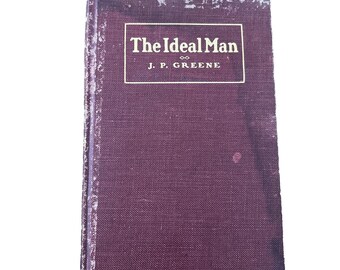 May include: A vintage hardback book with a worn, deep purple fabric cover. The front cover features a rectangular border containing the text The Ideal Man and J. P. Greene in cream-coloured lettering. The edges show significant wear and fading.