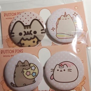 Puede incluir: Cuatro chapas redondas con ilustraciones de gatos de dibujos animados sobre tarjetas de soporte color melocotón etiquetadas como BUTTON PINS. Las chapas muestran un gato con una galleta, un gato con cuerno de unicornio, un gato con luna y un gato con cereza.