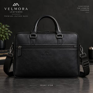 Puede incluir: Un maletín de cuero negro con dos asas superiores, una correa de hombro desmontable y un bolsillo frontal con cremallera. El bolso muestra el logotipo y texto de Velmora, junto a Sleek design for a smarter tomorrow y Front view.