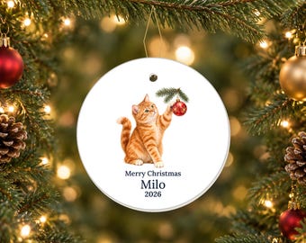 May include: A round white ceramic Christmas ornament featuring an illustration of an orange tabby cat reaching up to touch a red bauble hanging from a pine branch. The text reads Merry Christmas, Milo, and the year 2026 in dark blue font.