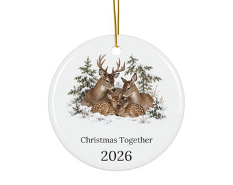 May include: A round white ceramic ornament hanging from a gold string. The center features a detailed illustration of a deer family resting in a snowy forest. Below the deer, the text reads Christmas Together and the year 2026 in black font.