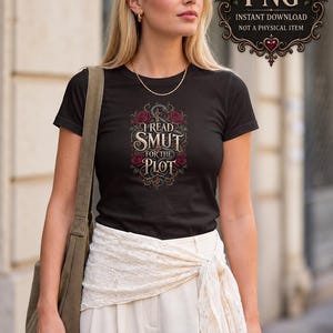 May include: A black short-sleeved t-shirt featuring a graphic design with the text I READ SMUT FOR THE PLOT, surrounded by red roses and a dark serpent. The shirt is paired with white trousers and a white lace waist wrap, with an olive green bag.