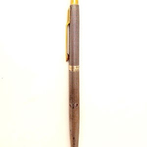 May include: A silver-toned ballpoint pen featuring a fine grid pattern across its cylindrical body. The pen includes a gold-coloured clip and a matching gold-coloured top cap. A small, metallic band separates the upper and lower sections.