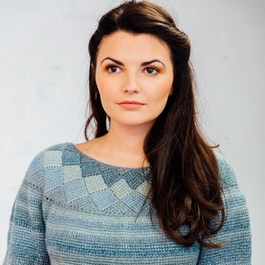 Puede incluir: Un suéter de punto azul y gris a rayas con un patrón geométrico alrededor del cuello. El suéter tiene mangas largas y un corte holgado.