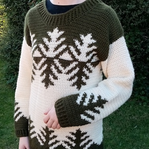 May include: A green and white crocheted sweater with a snowflake pattern. The sweater has long sleeves and a crew neck.