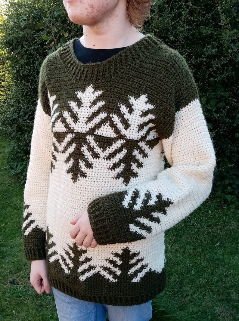 May include: A green and white crocheted sweater with a snowflake pattern. The sweater has long sleeves and a crew neck.