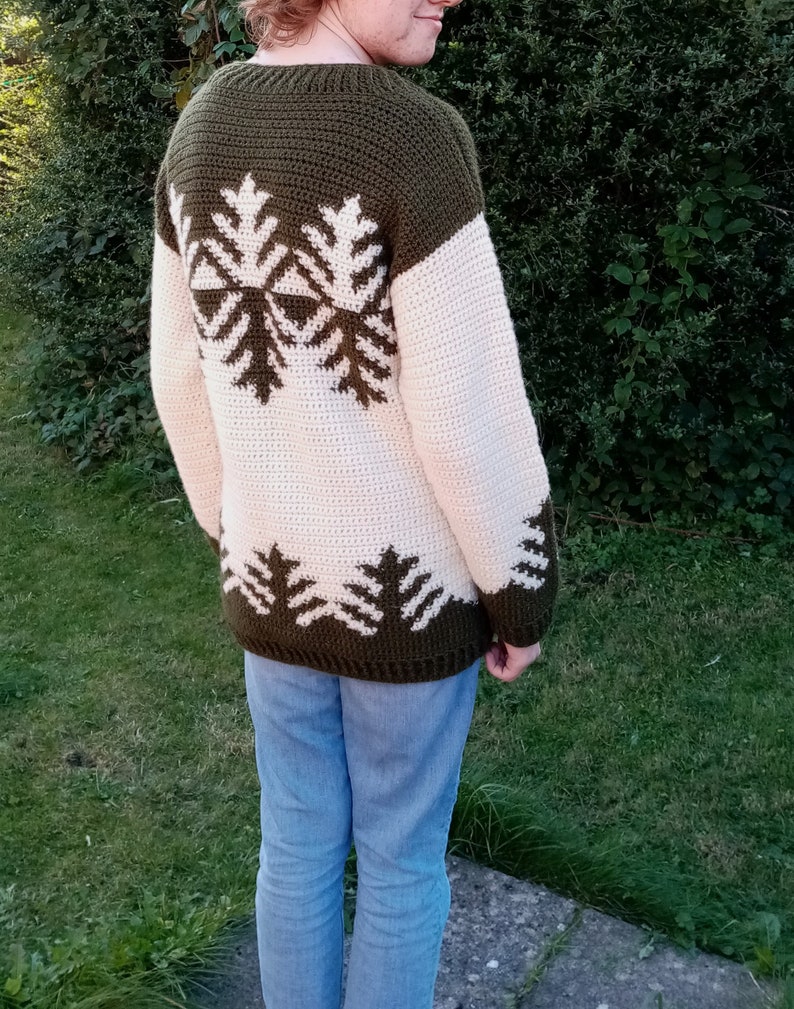 May include: A green and cream crocheted sweater with a snowflake design on the back.