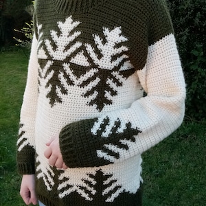 May include: A green and white crocheted sweater with a snowflake pattern. The sweater has long sleeves and a crew neck.