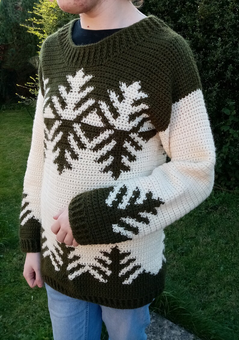 May include: A green and white crocheted sweater with a snowflake pattern. The sweater has long sleeves and a crew neck.