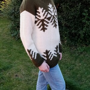 May include: A crocheted sweater with a white and green snowflake pattern. The sweater has a crew neck and long sleeves.