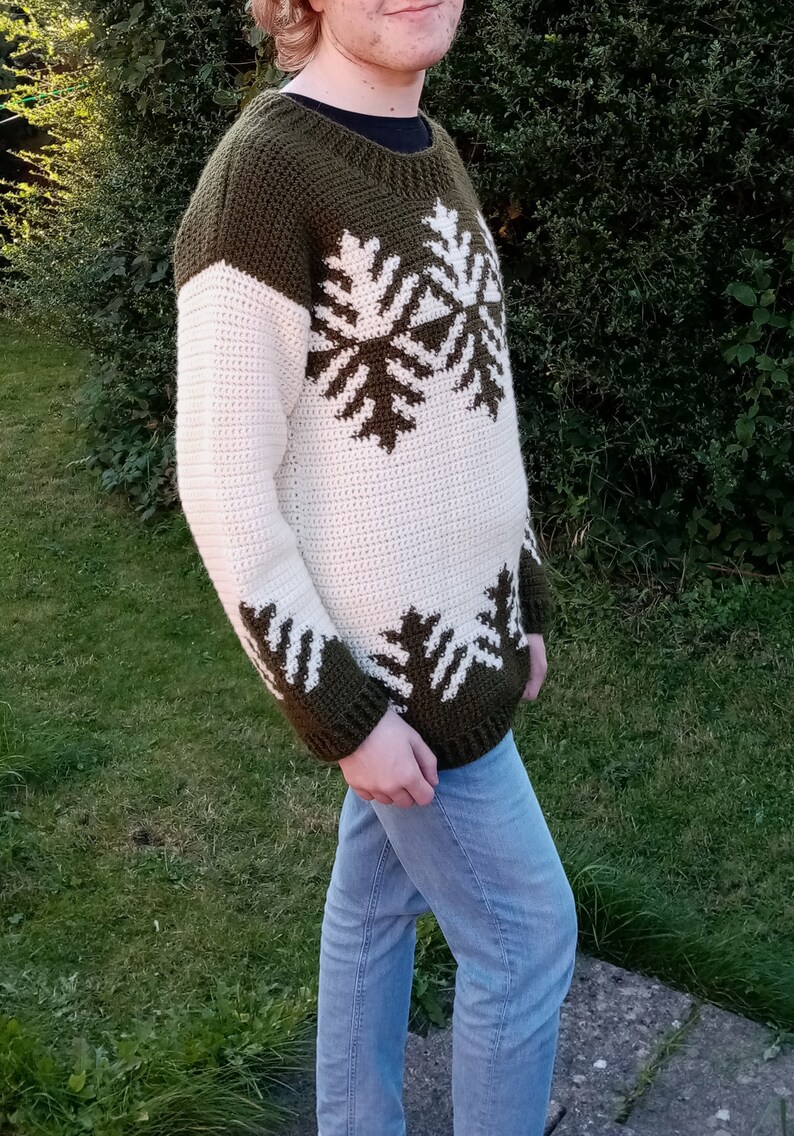 May include: A crocheted sweater with a white and green snowflake pattern. The sweater has a crew neck and long sleeves.