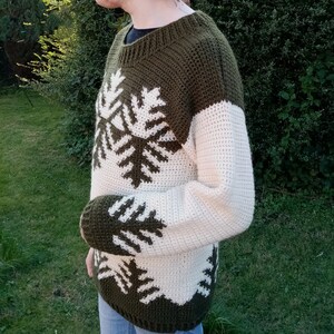 May include: A green and white crocheted sweater with a snowflake pattern. The sweater has long sleeves and a crew neck.