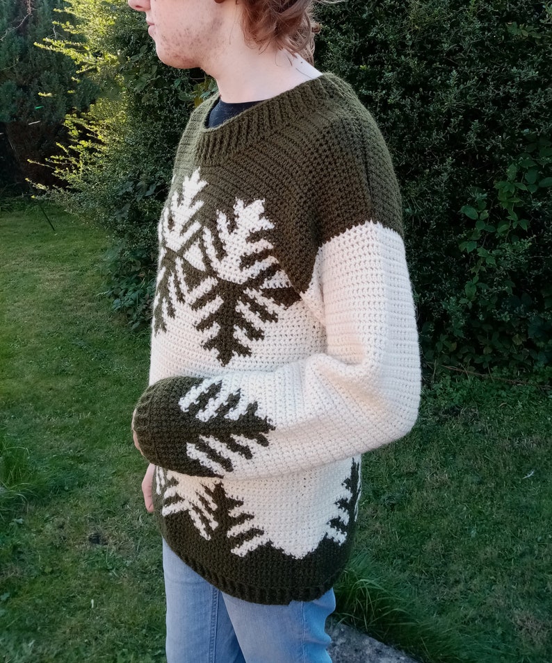 May include: A green and white crocheted sweater with a snowflake pattern. The sweater has long sleeves and a crew neck.