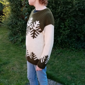 May include: A crocheted sweater with a white and green snowflake pattern. The sweater has long sleeves and a crew neck.