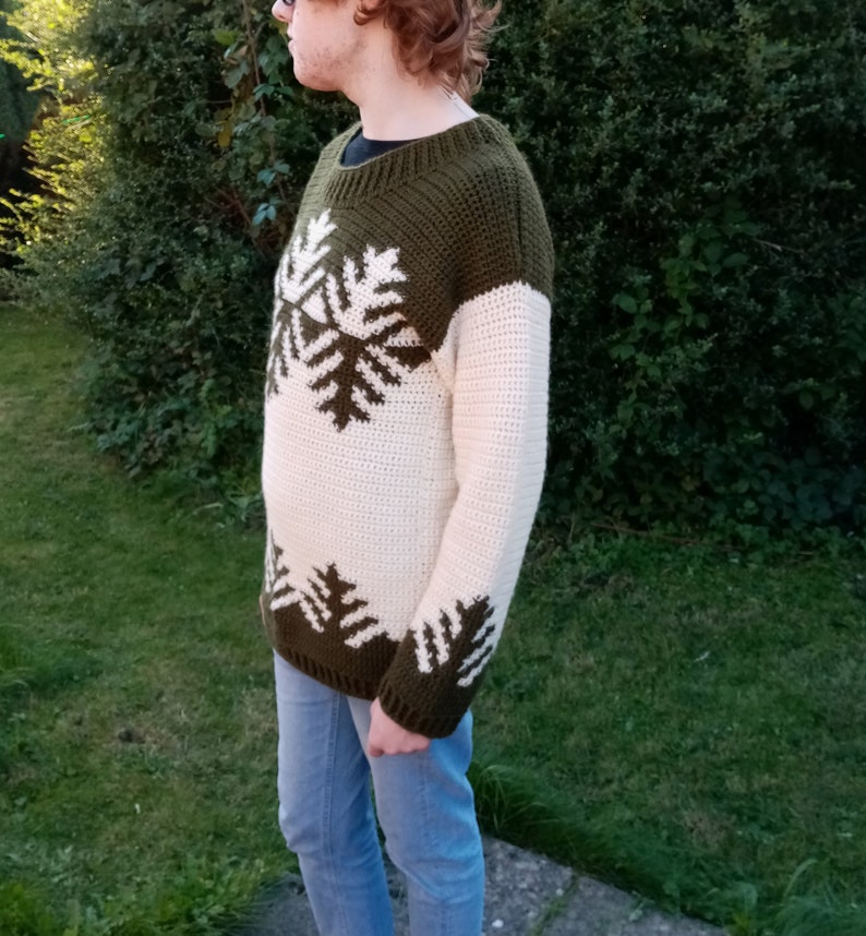 May include: A crocheted sweater with a white and green snowflake pattern. The sweater has long sleeves and a crew neck.