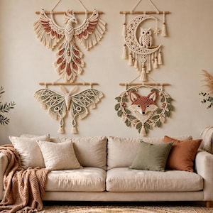 May include: Four macrame wall hangings featuring a phoenix, a crescent moon with an owl, a moth, and a fox face surrounded by leaves. Each piece is crafted from cream-coloured cord with accents in rust, sage green, and brown, suspended from wooden dowels.