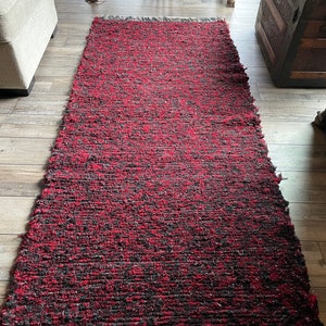 May include: A red and black woven rug with fringe on the ends. The rug is made of a thick, textured material and has a slightly distressed look.