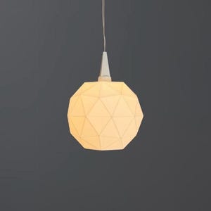 Könnte beinhalten: Eine kugelförmige Pendelleuchte mit einer weißen, facettierten geometrischen Oberfläche aus dreieckigen Paneelen. Die Lampe hängt an einem dünnen Kabel, das an einer weißen konischen Halterung befestigt ist und ein warmes Licht abgibt.