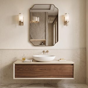 May include: A wall-mounted bathroom vanity featuring a dark wood drawer front, a light-colored countertop, and a white vessel sink. Above the vanity is a rectangular mirror with rounded corners, flanked by two cylindrical wall sconces.