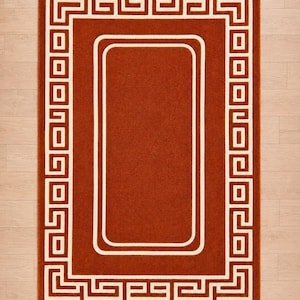 Puede incluir: Una alfombra rectangular con un centro de color naranja quemado sólido y un borde ancho. El borde muestra un patrón geométrico griego blanco que consiste en líneas y cuadrados entrelazados que enmarcan todo el perímetro.