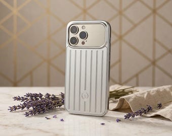 Op de afbeelding: Een zilverkleurige telefoonhoes met een verticaal gegroefde textuur en een glad metalen paneel rond de cameralenzen. De hoes is voorzien van een klein rond logo in het midden onderaan en is ontworpen voor een smartphone met drie lenzen.