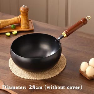 May include: A black round-bottomed wok with a long brown wooden handle featuring a gold-coloured metal ring at the end. The wok has a diameter of 28 cm without a cover. The cooking vessel is positioned on a round woven mat on a wooden surface.