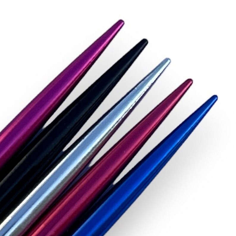 May include: Five knitting needles with pointed tips in different colors: purple, black, silver, pink, and blue.