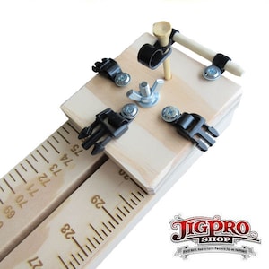Puede incluir: Un jig de madera con una regla y un tee de golf en el centro. El jig tiene cuatro abrazaderas negras y una tuerca y un tornillo de metal. El jig est&aacute; etiquetado como "JigPro Shop".