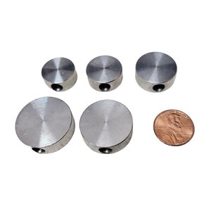 May include: Five silver metal round discs with a hole in the center. The discs are different sizes and are arranged in a row. A penny is placed below the discs for size comparison.